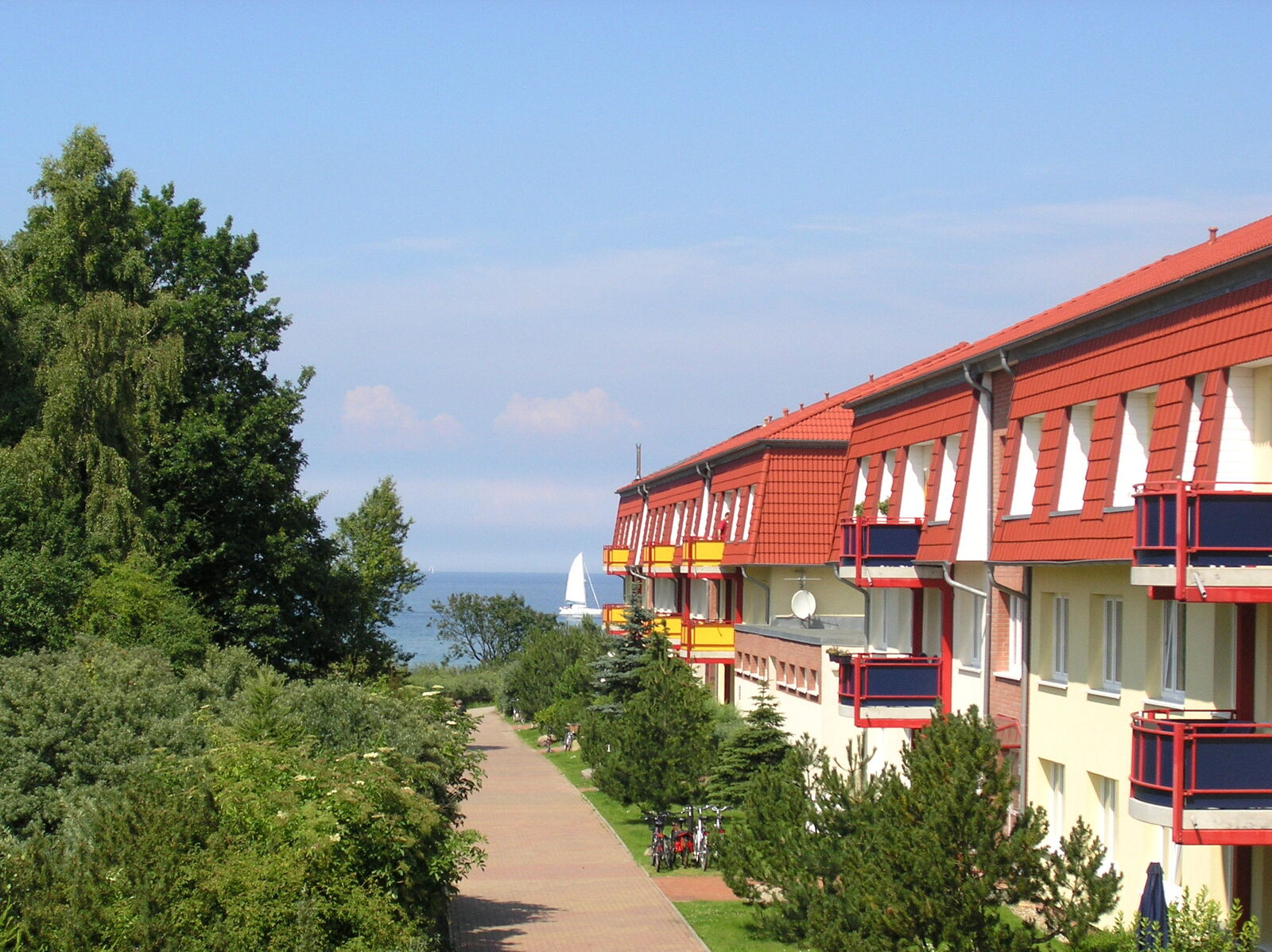 Ferienanlage Dünengarten in Kühlungsborn mit rot-weißen Fassaden, Balkonen und Weg Richtung Ostsee