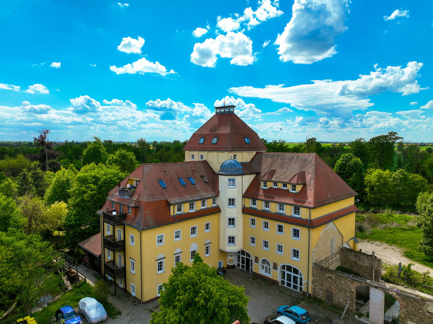 Luftaufnahme der Schlossmühle Walda mit gelber Fassade, Mühlenturm und Innenhof an einem sonnigen Tag